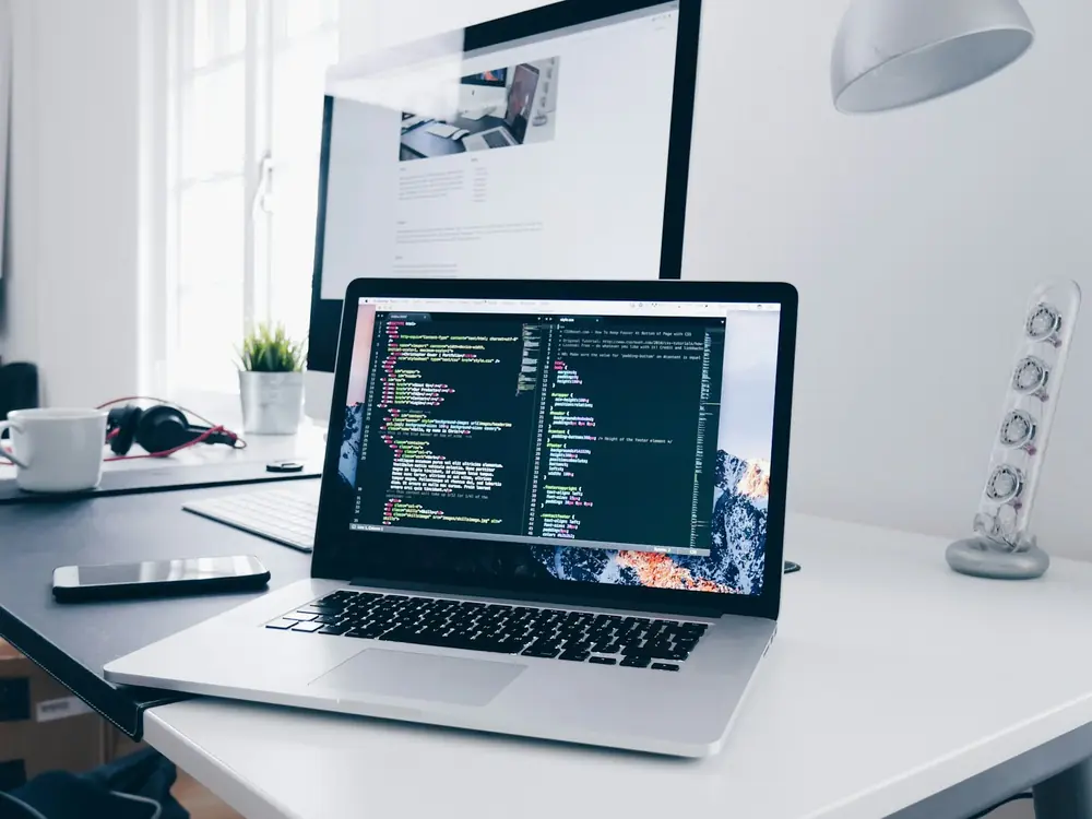 Desk with a laptop showing code and a monitor